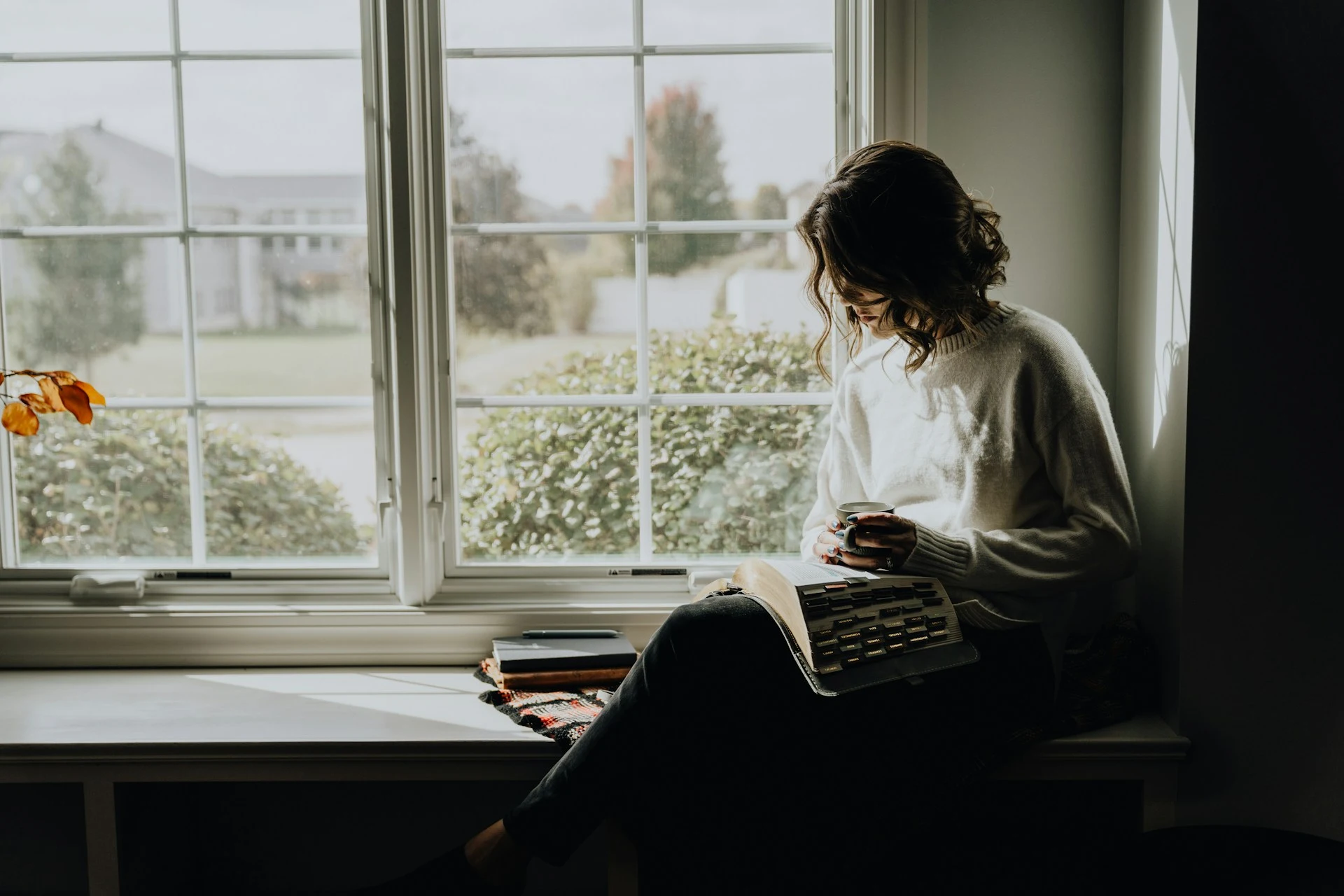 mujer adulta leyendo junto a la ventana con una taza de café, disfrutando la tranquilidad de vivir sola al independizarse